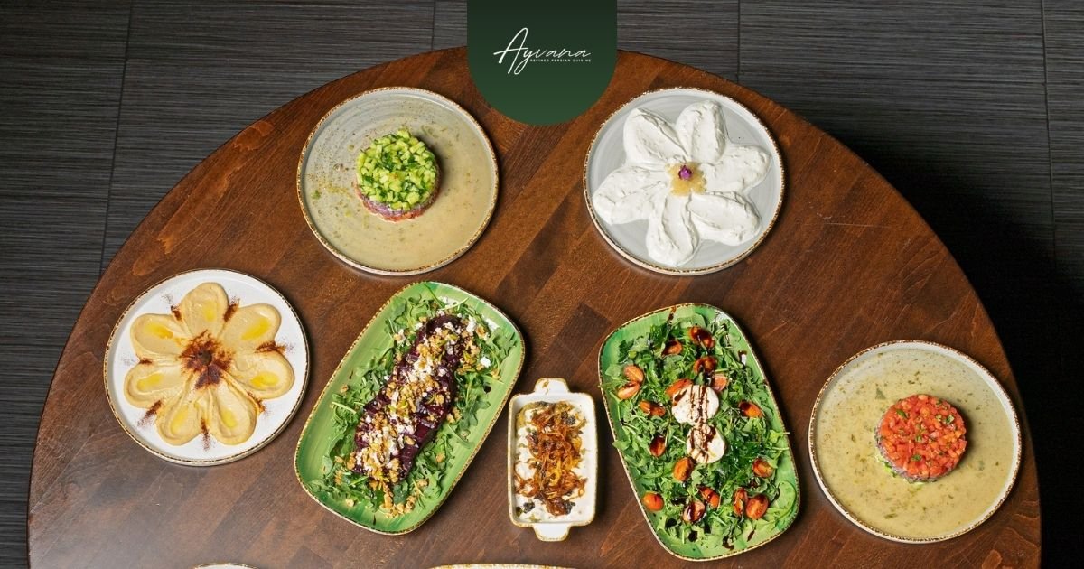 Vibrant Persian feast on a round wooden table featuring Shirazi salad, creamy dips, herb platters, and elegant garnishes at Ayvana restaurant.