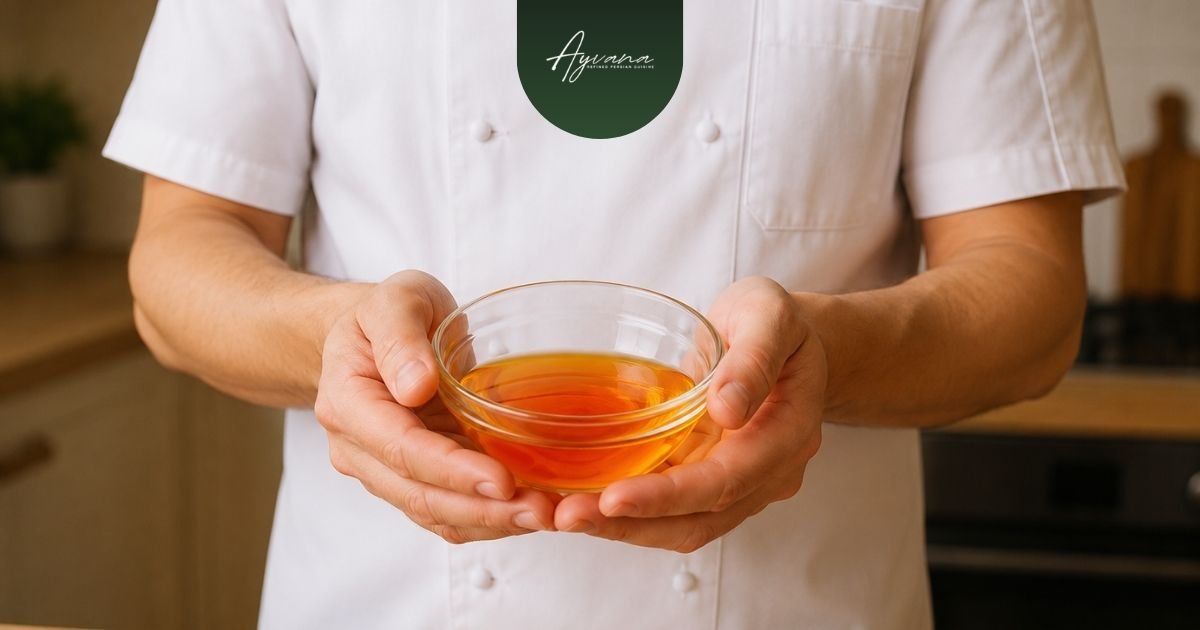 Chef holding bowl of saffron infusion inside warmly lit professional kitchen preparation setting.