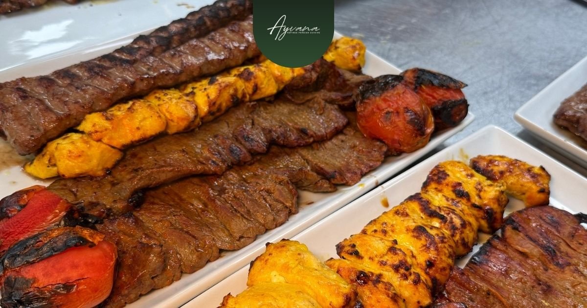 Assortment of Persian kebabs including koobideh, barg, joojeh, and grilled tomatoes with saffron chicken and beef on white platters at Ayvana.