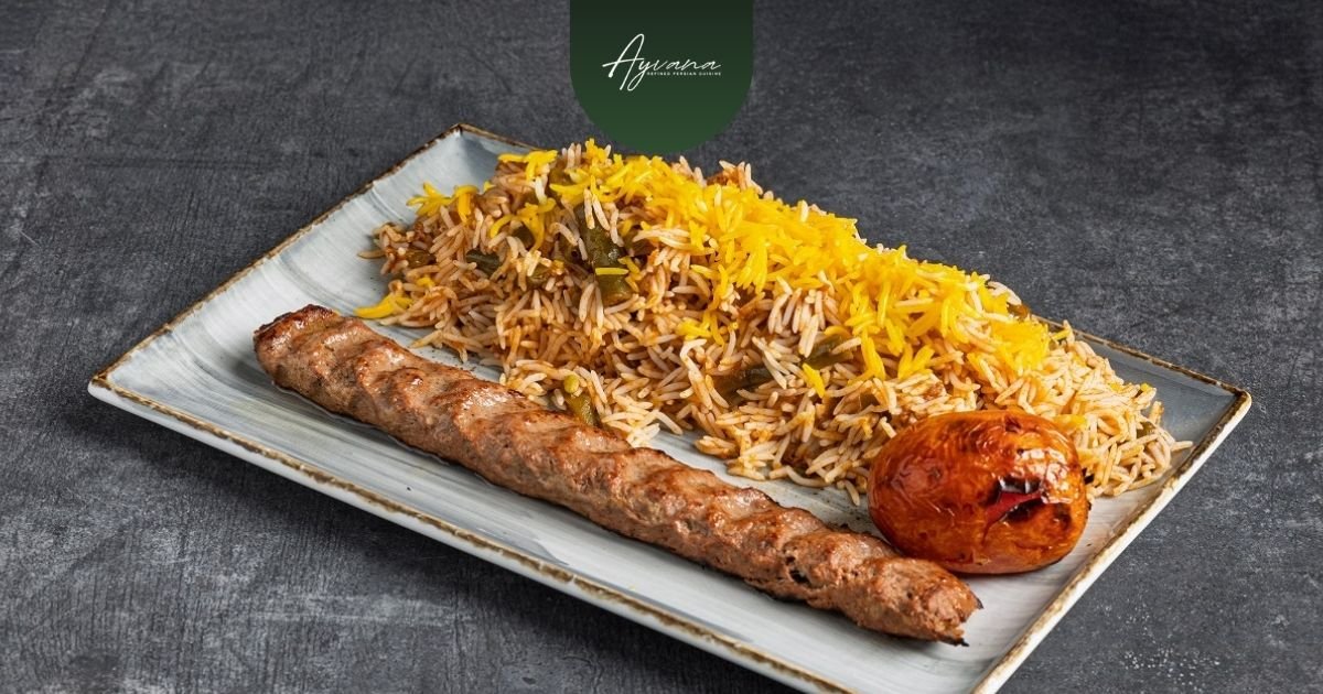 Grilled koobideh kebab served with saffron rice and a roasted tomato on a white plate, classic Persian presentation.