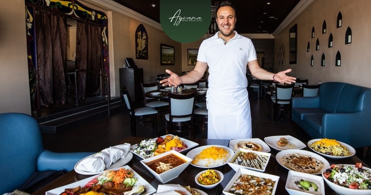 Chef presenting a large table filled with colorful traditional Persian dishes at Ayvana Restaurant.