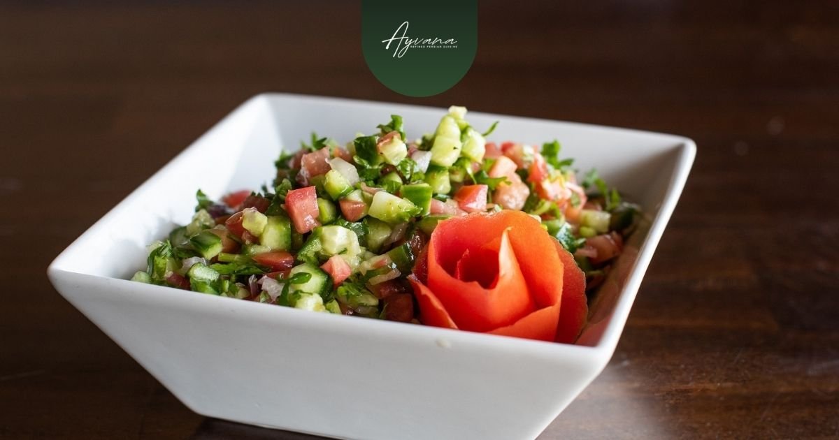 Molded Shirazi salad with finely diced cucumbers, tomatoes, and onions layered on a creamy sauce, served on a rustic plate at Ayvana.